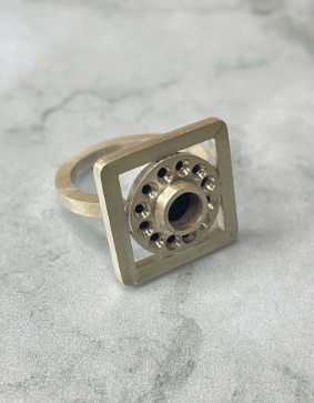 Ce projet de bague a été réalisé en plusieurs étapes. L’anneau a d’abord été ouvert, puis deux fleurs de rupture ont été ajoutées sur le haut afin de soutenir le reste de la pièce. Au-dessus, une coupole formée par emboutissage est surmontée de mises en pierre et d’un serti clos. Enfin, un carré, fabriqué à partir d’un fil carré plié et orné de fleurs de rupture, vient entourer la coupole.